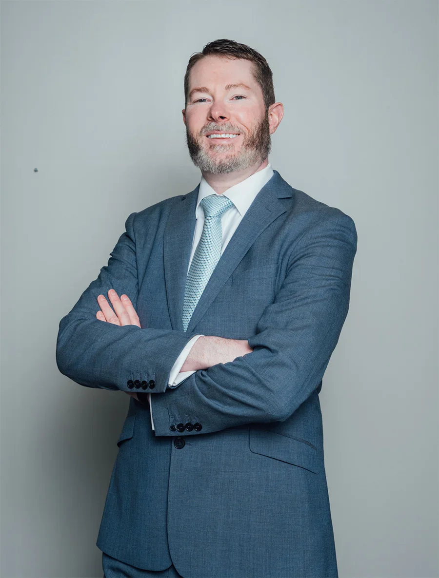 Portrait shot of Dr. Andrew Compton MD smiling at the camera. He wears a light navy suit, white under shirt and a light teal tie.